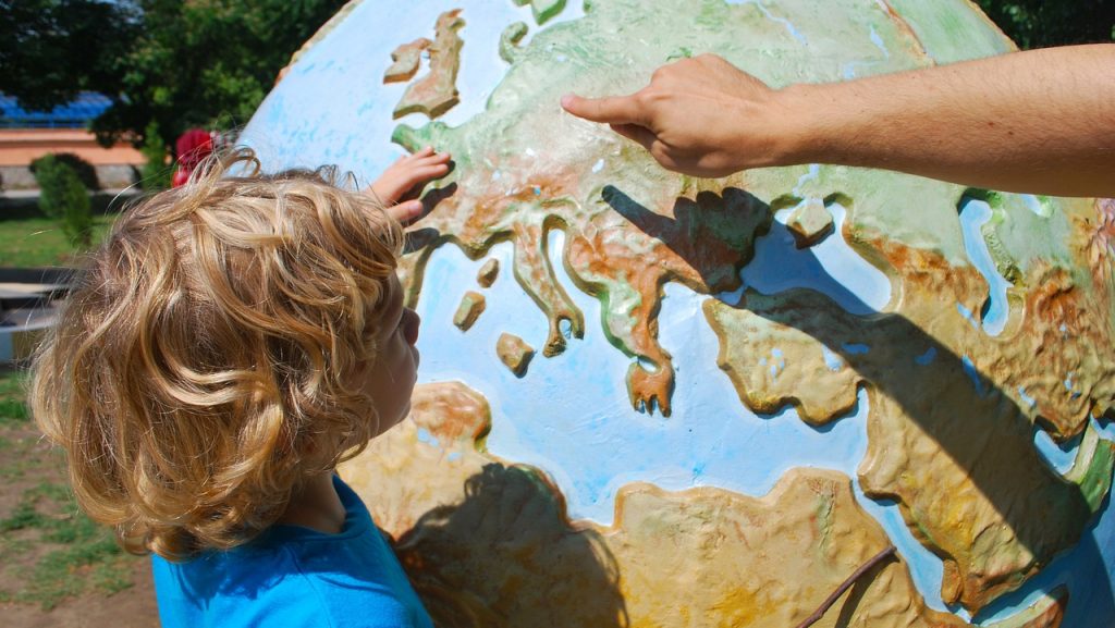 Adulto enseñándole las diferentes zonas, climas, y nombres de los continentes a un niño en una bola terráquea gigante