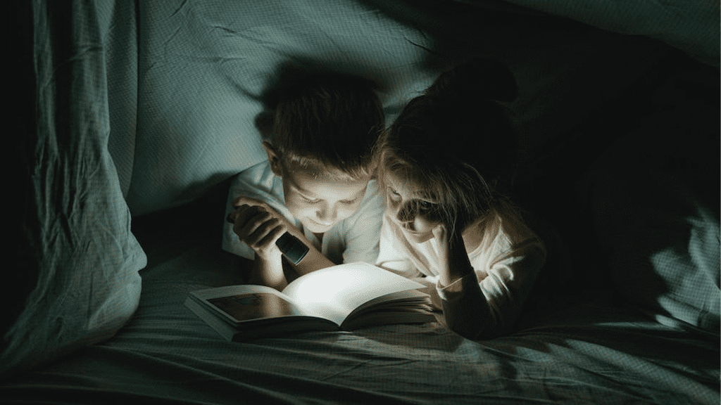Niños leyendo un cuento bajo las sábanas